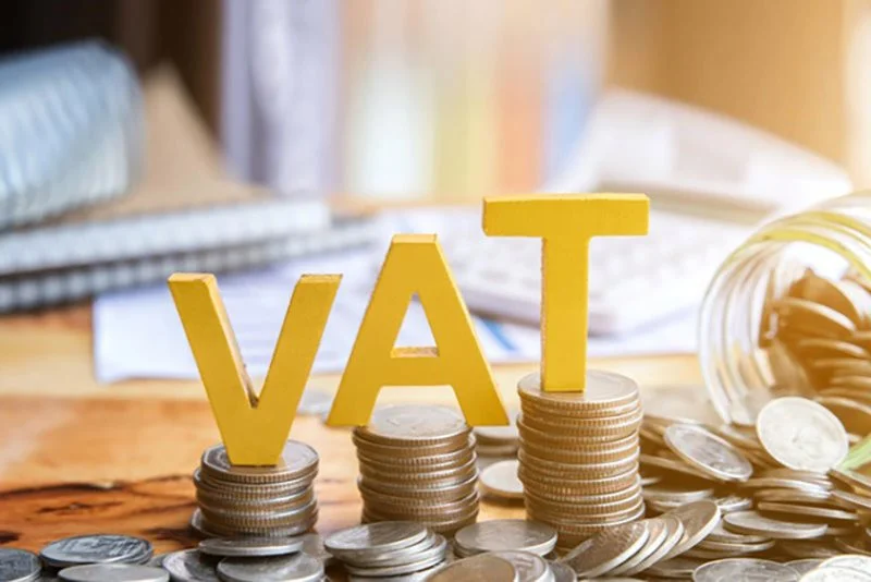 Chữ VAT màu vàng đặt trên tiền xu bên cạnh lọ thủy tinh