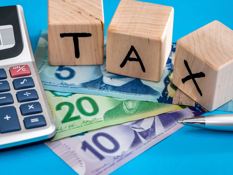 Chữ TAX bằng khối gỗ cạnh máy tính và tiền giấy