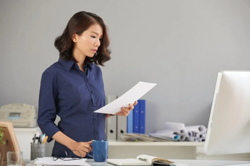 Nhân viên văn phòng đọc tài liệu bên máy tính