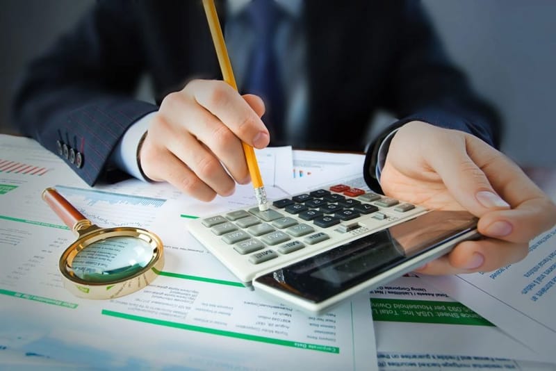 Tay cầm bút và máy tính rà soát số liệu, bên cạnh kính lúp